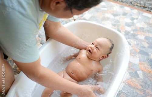 4 month old Asian baby boy having bath in tubby on Father's hand.