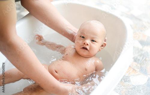 4 month old Asian baby boy having bath in tubby on Father's hand.