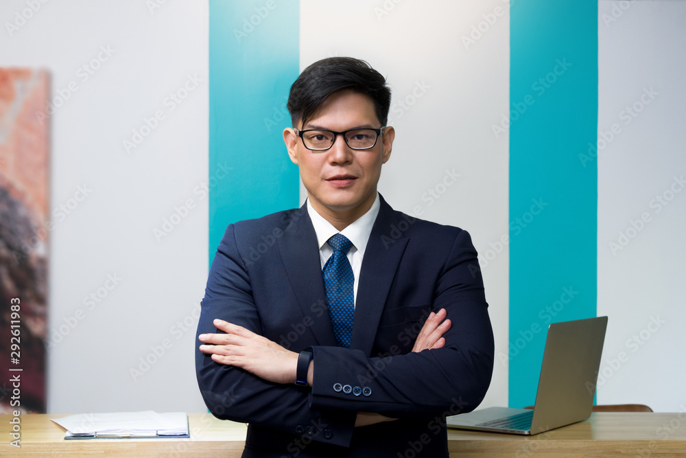 A business person car rental operator or lodging wearing blue suit and glasses is standing with arms crossed in front of the counter. Portrait of businessman. A business person car rental operator or lodging wearing blue suit and glasses is standing with arms crossed in front of the counter. Portrait of businessman.