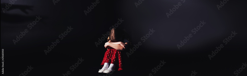 panoramic shot of depressed child sitting with bowed head on black background