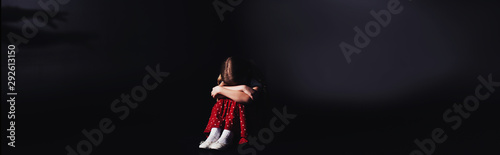 panoramic shot of depressed child sitting with bowed head on black background