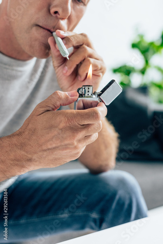 cropped view of man in t-shirt lighting up blunt with medical cannabis