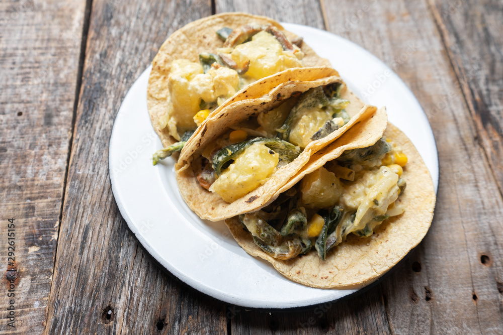 Mexican tacos of poblano rajas with potatoes and sour cream on wooden background