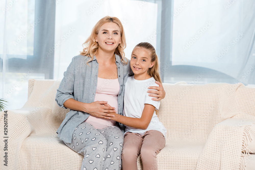 happy daughter touching belly of pregnant mother at home
