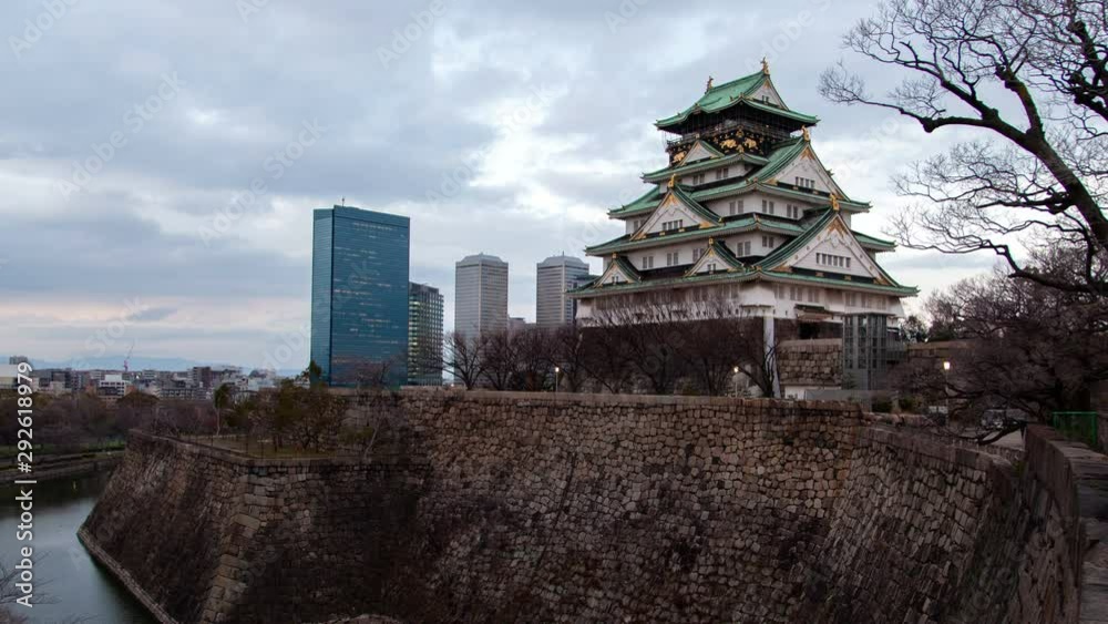 Time lapse zoom out Osaka ancient landmark tourist attraction of samurai fortress with defence wall and feudal castle with museum against city skyscrapers from evening till illuminated night Time lapse zoom out Osaka ancient landmark tourist attraction of samurai fortress with defence wall and feudal castle with museum against city skyscrapers from evening till illuminated night