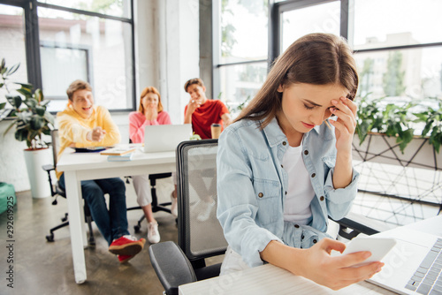 laughing schoolchildren bullying sad girl with smartphone in school photo