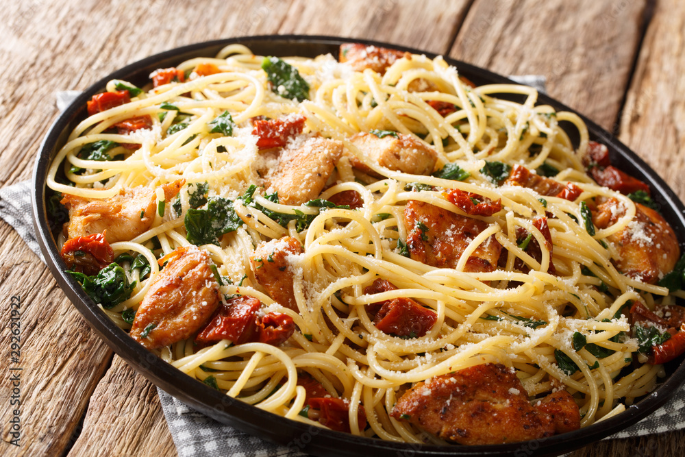 Cooked spaghetti with dried tomatoes, pieces of chicken, parmesan and spinach close-up on a plate. horizontal Cooked spaghetti with dried tomatoes, pieces of chicken, parmesan and spinach close-up on a plate. horizontal