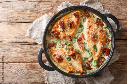Main course baked chicken with sun-dried tomatoes and spinach in cheese sauce close-up in a pan. Horizontal top view