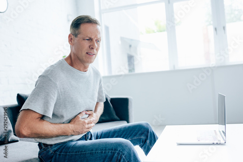 handsome man in t-shirt with stomachache sitting on sofa photo