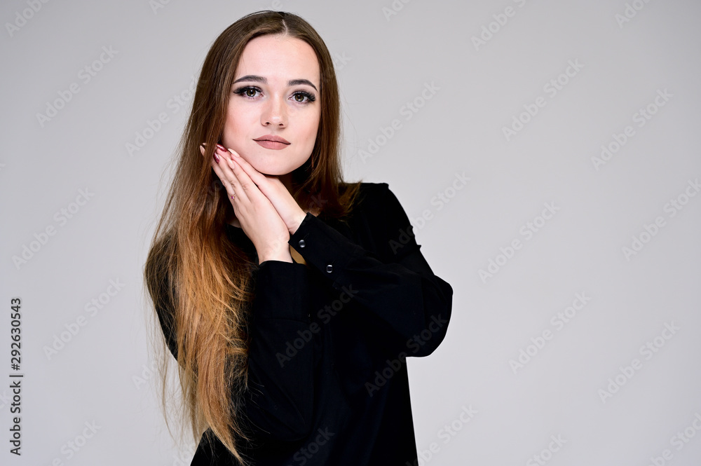 Portrait of a pretty brunette girl with beautiful hair, excellent make-up, beautiful face skin in a black blouse on a light gray background. Made in the studio. Portrait of a pretty brunette girl with beautiful hair, excellent make-up, beautiful face skin in a black blouse on a light gray background. Made in the studio.