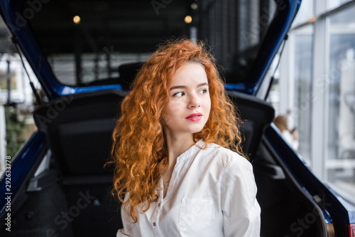 Portrait of a beautiful red-haired girl on the background of the car