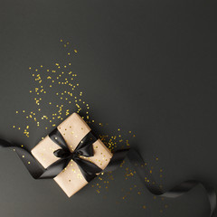 Gift or present box and gold stars confetti on black table top view. Flat lay composition for birthday, mother day, black friday sale, xmas, christmas, new yaer or wedding.