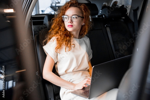 Business lady in glasses sitting inside the car with a laptop © pantovich