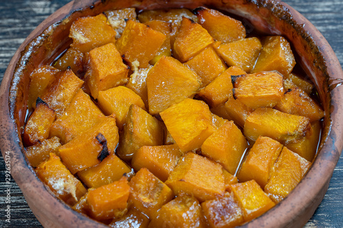 Baked yellow pumpkin with honey, olive oil and spices on a plate on the wooden table. Vegetarian food. Closeup