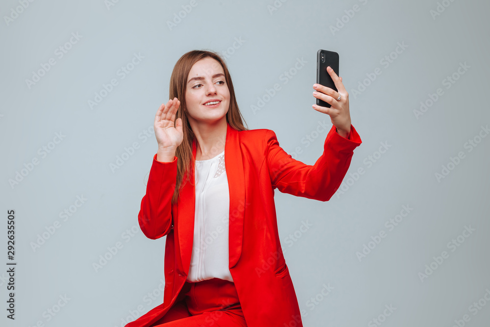 Naklejka premium girl in a red jacket takes a selfie on the phone on a gray background