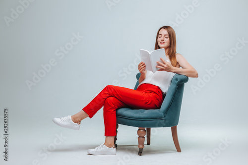 Girl in red pants sitting in a chair and reading a book with a white cover