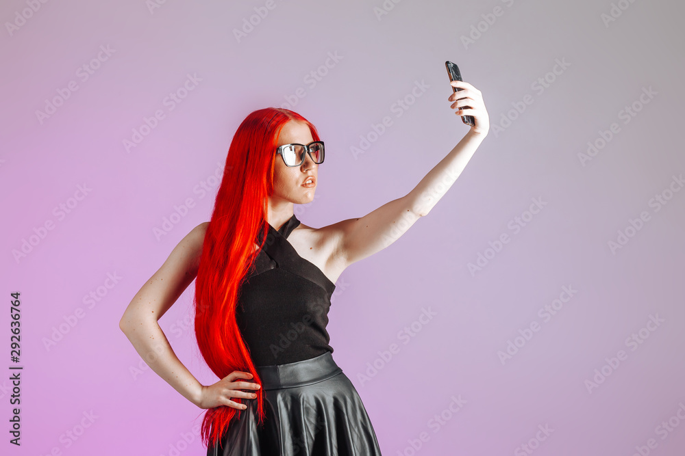 A girl with red long hair wearing glasses and a leather skirt takes a selfie on a pink background A girl with red long hair wearing glasses and a leather skirt takes a selfie on a pink background