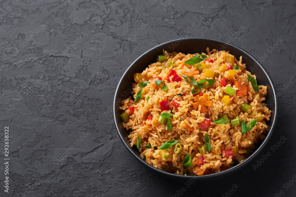 Veg Schezwan Fried Rice in black bowl at dark slate background. Vegetarian Szechuan Rice is indo-chinese cuisine dish with bell peppers, green beans, carrot. Veg Schezwan Fried Rice in black bowl at dark slate background. Vegetarian Szechuan Rice is indo-chinese cuisine dish with bell peppers, green beans, carrot.