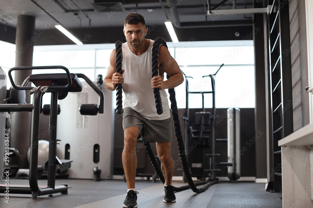 Fototapeta premium Athletic młody człowiek z liny bojowej robi ćwiczenia w siłowni fitness trening funkcjonalny.