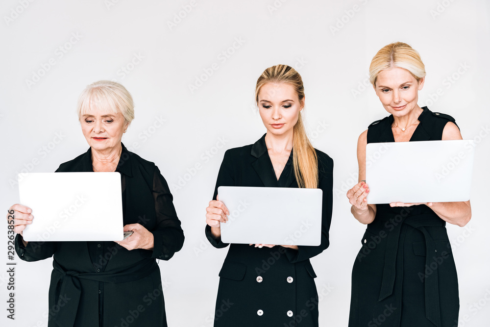 fashionable three-generation blonde businesswomen in total black outfits with laptops isolated on grey fashionable three-generation blonde businesswomen in total black outfits with laptops isolated on grey