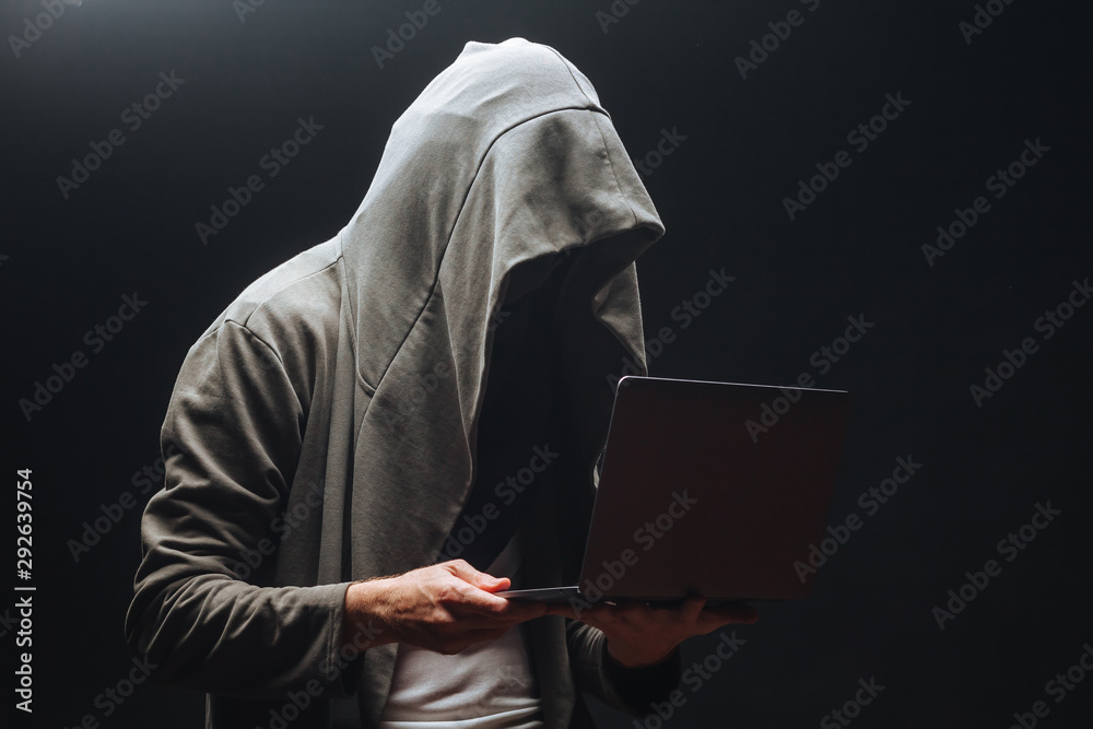 Criminal with laptop in hood at night Criminal with laptop in hood at night