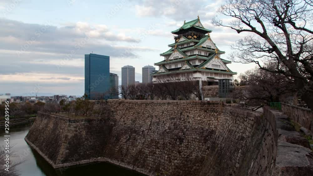 Timelapse zoom out Osaka famous world tourist attraction of ancient samurai castle with defence fortification stone wall by river against city skyscrapers under cloudy sky from morning till evening Timelapse zoom out Osaka famous world tourist attraction of ancient samurai castle with defence fortification stone wall by river against city skyscrapers under cloudy sky from morning till evening
