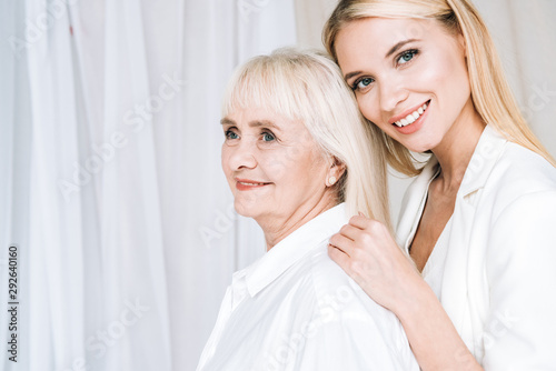 close-up of elegant blonde granddaughter hugging smiling grandmother