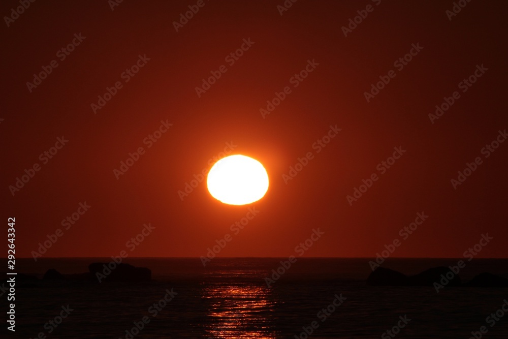 sun reaching the horizon in the sea on a red sky sunset