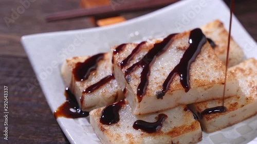 Pouring black soy sauce on ready-to-eat delicious turnip cake, Chinese traditional local dish radish cake in restaurant, close up, 4K resolution shot. photo