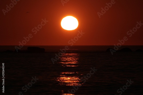 sun reaching the horizon in the sea on a red sky sunset