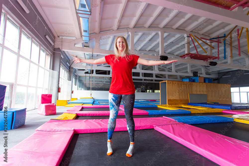 Fitness, fun, leisure and sport activity concept - Young happy woman jumping on a trampoline indoors Fitness, fun, leisure and sport activity concept - Young happy woman jumping on a trampoline indoors