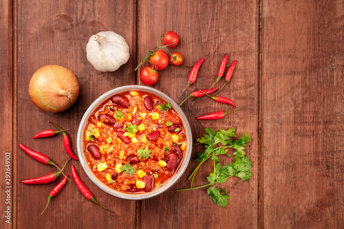 Chili con carne, shot from above on a dark rustic wooden background with ingredients and a place for text