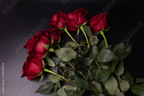 dark red roses with green leaves in a bouquet lie on a table on a dark gray background