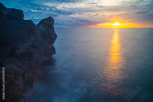 Beautiful Menorca/Minorca sunset with reflection of sun in sea, rock formation to side and dramatic cloud formation.