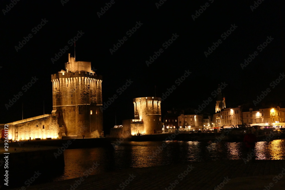 Naklejka premium La Rochelle old port (Vieux Port) lit up at night, showing Tour Saint Nicholas (on the left) and Tour de la Chaine (on the right) guarding the entrance to the harbour