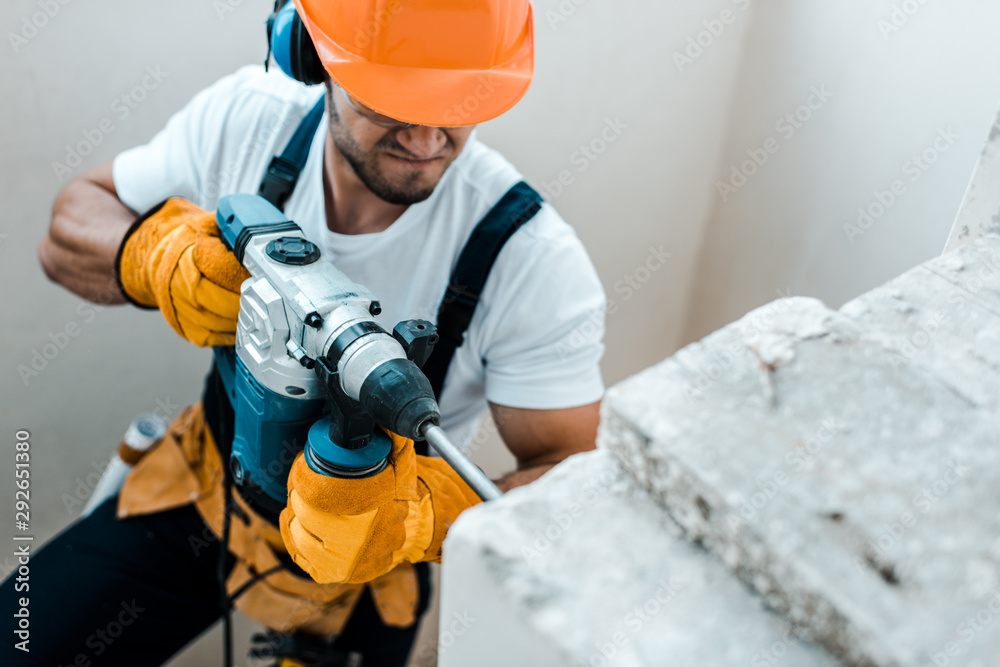 overhead view of handyman in helmet and yellow gloves using hammer drill