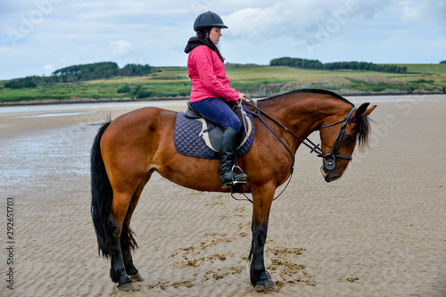 Young woman riding her horse on a deserted beach 
