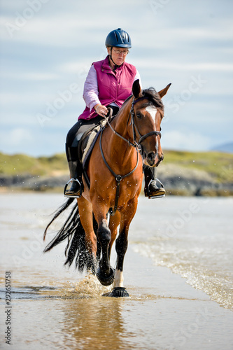 Woman riding her horse down the breakwater on the beach. 