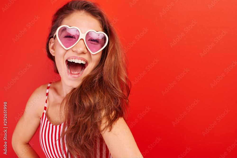 Fototapeta premium Portrait of cheerful asian kazakh young woman in summer glasses dressed casual smiling joyfully isolated on red with copy space