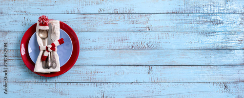 Christmas table setting with holiday decorations in the form of a knitted hat and scarf in white and red on an old wooden background with copy space.