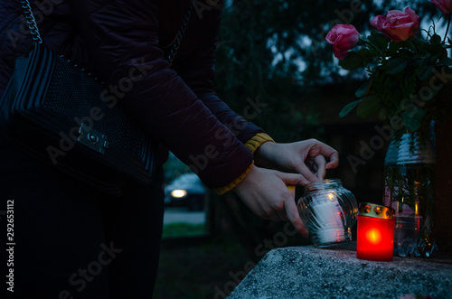 Woman light on red and yellow candles in the dark - to put them on a tombstone - all souls day preparing in the cemetery