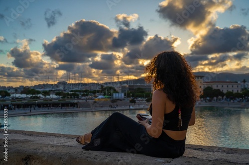 Young caucasian brunette woman with curly hair and dreadlocks sitting while playing kalimba on sunset © Daniel