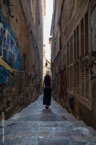 Young caucasian brunette woman with curly hair and dreadlocks walking through a narrow street at the city old town