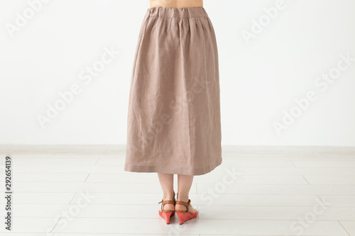 Young unidentified girl in a brown long skirt and shoes stands neara white wall. The concept of feminine design products
