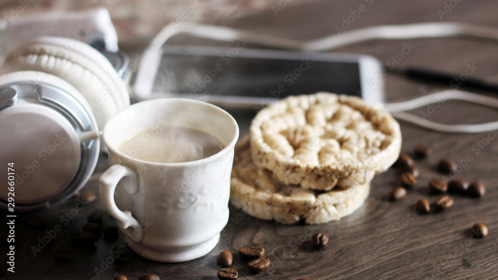 A Cup of coffee and round loaves, large white headphones and a smartphone on a wooden table A Cup of coffee and round loaves, large white headphones and a smartphone on a wooden table