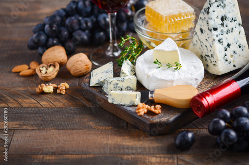 Cheese plate with grapes, honey, nuts and red wine on a wooden table.