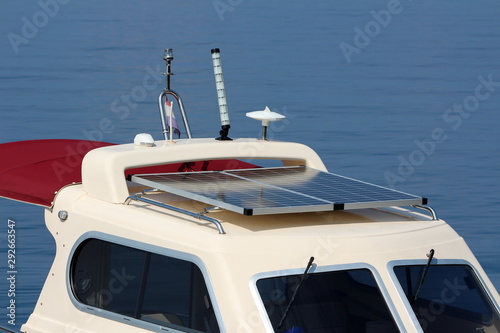 Modern new solar panels on top of small white and dark red boat next to multiple electronic gadgets from signal light to sensors surrounded with calm sea on warm sunny summer day photo