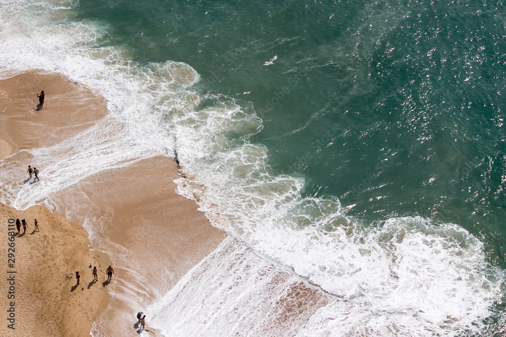 Drone view of people on the yellow sand beach facing the Beautiful crushing waves of Atlantic ocean in Nazare, Portugal	