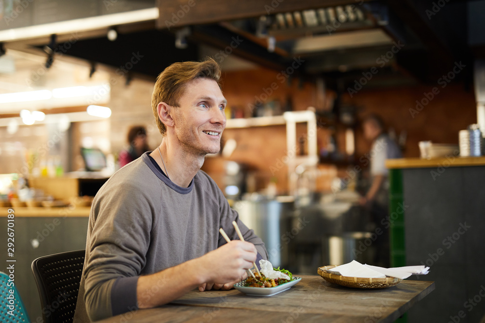 Portrait of smiling adult man enjoying Asian food sitting at table in cafe or restaurant, copy space