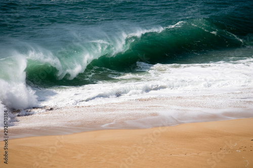 Beautiful crushing wave of Atlantic ocean, captured during the walk along the sandy beach in Nazare, Portugal